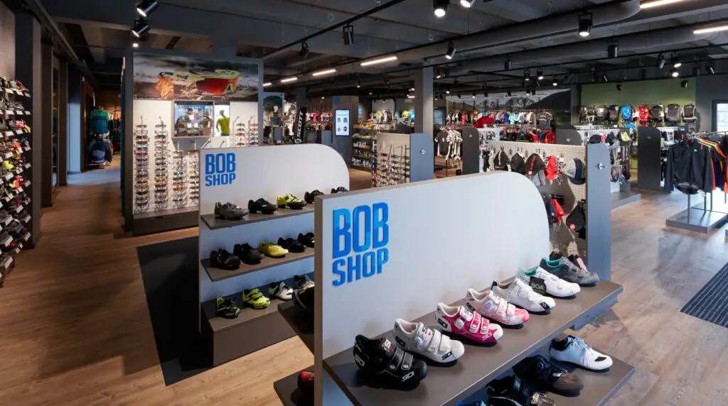 Gut beleuchtetes Geschäft mit sportlichen Schuhen, Kleidung, Helmen und Sonnenbrillen, Beschriftung "BOB SHOP".
