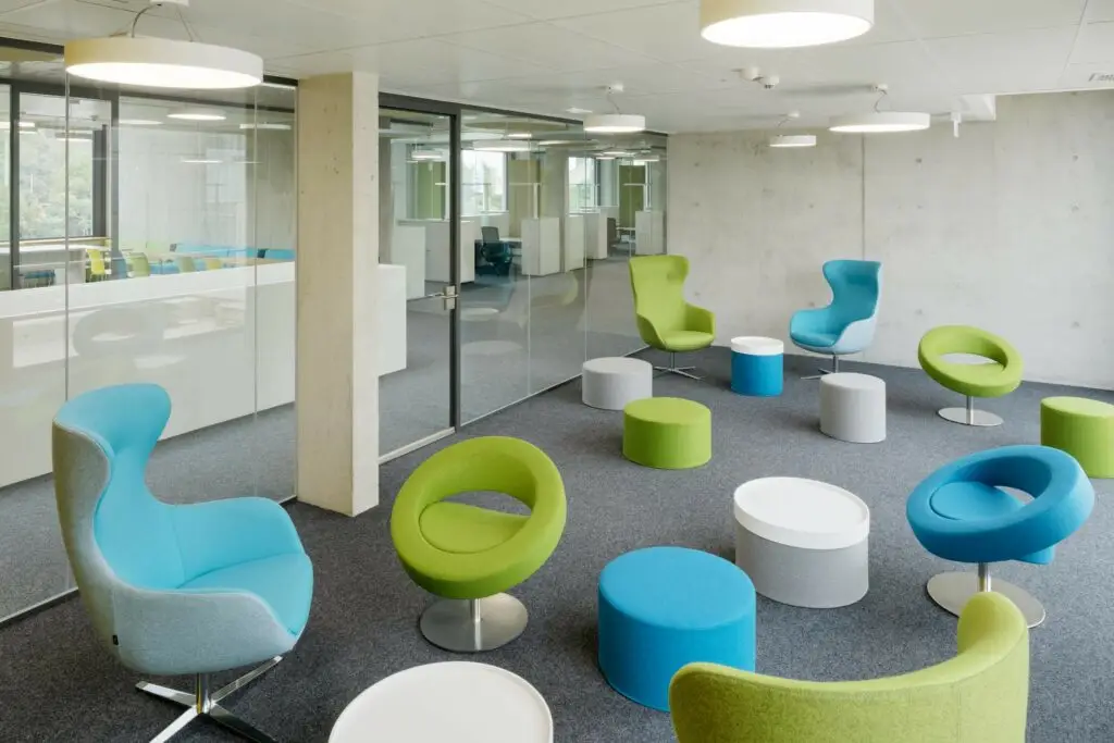Modernes Büro mit Glaswänden, bunten ergonomischen Stühlen, runden Hockern und heller Beleuchtung.