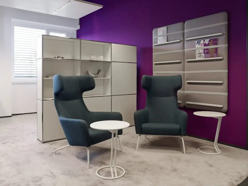 Modernes Zimmer mit zwei blauen Sesseln, einem kleinen Tisch, lila Wand und Regalen.